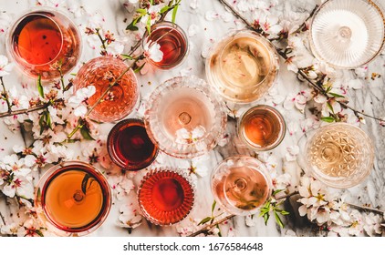 Various shades of rose wine. Flat-lay of rose wine in different colors in glasses and spring blossom flowers over marble background, top view. Wine shop, bar, tasting, seasonal wine list concept