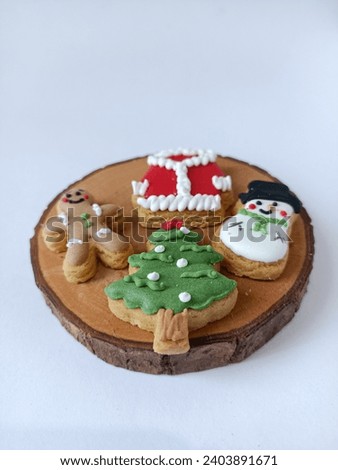 Various shapes of typical Christmas cookies, gingerbread man, santa's red clothes, snowman and christmas trees as selective focus on wooden coaster on a white background