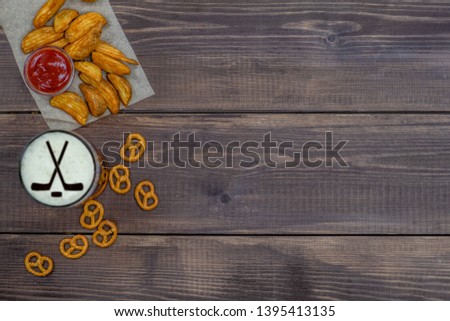 Various snacks and beer with silhouettes of hockey sticks on beer foam on dark wooden background. Top view, Empty space for text.