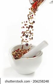 Various Spices Falling Into Mortar And Pestle On A White Background