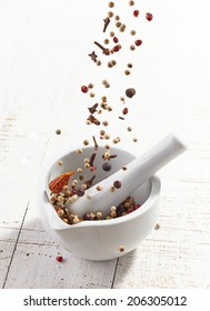 Various Spices Falling Into Mortar And Pestle On White Wooden Table