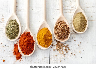various spices in wooden spoons on old white wooden table