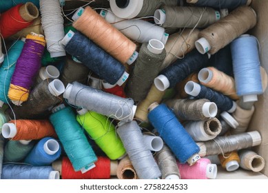 Various spools of multicolored sewing thread filling a box, creating a textile background for craft and fashion concepts