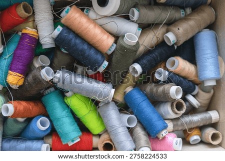 Various spools of multicolored sewing thread filling a box, creating a textile background for craft and fashion concepts