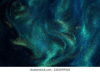 Various stains and overflows of gold particles in blue fluid with green tints. Golden particles dust and smooth defocused background. Liquid iridescent shiny backdrop with depth of field.
