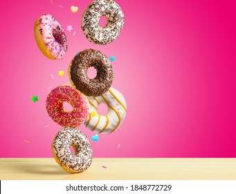 Various sweet doughnuts with sprinkel on pink red background falling on the table. Copy space