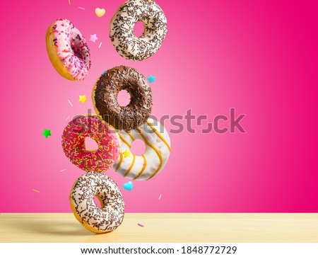 Various sweet doughnuts with sprinkel on pink red background falling on the table. Copy space