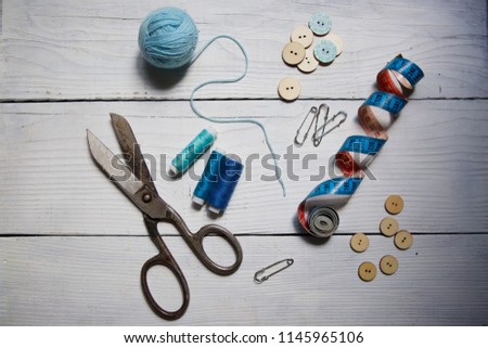 Various tools for sewing, hobby and creativity lie on the white wooden surface. Measuring tape, scissors, buttons, thread and other elements. The view from the top.