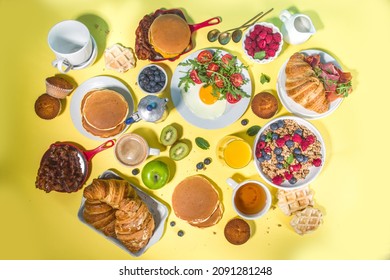 Various traditional breakfast food - fried eggs with bacon, muesli, oats, waffles, pancakes, burger, croissants, fruit berry, coffee, tea and orange juice, yellow table background copy space top view