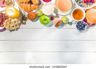 Various traditional breakfast food - fried eggs with bacon, muesli, oats, waffles, pancakes, burger, croissants, fruit berry, coffee, tea and orange juice, white table background copy space top view
