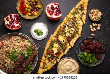 Various Turkish dishes: pide pizza, meat kebab with tabbouleh salad, falafel, hummus, olives, pistachios and Middle Eastern meze on black concrete table top view. Ethnic arab food, cuisine of Turkey - Shutterstock ID 1990588232