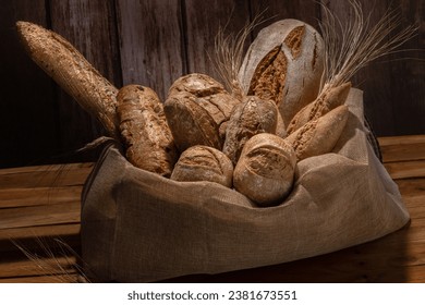 various types of artisan sourdough breads decorated with ears of wheat and placed in a raffia sack on a wooden table. - Powered by Shutterstock