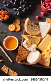 Various types of cheese in wooden box, honey, nuts, crackers, grapes and  berries on black concrete background