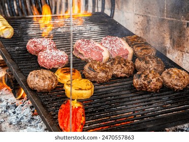 Various types of meat, pepper, bread and garlic bread being roasted in a typical Uruguayan grill called parrilla supplied with firewood and flames in a restaurant kitchen.