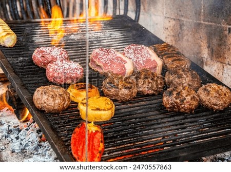 Various types of meat, pepper, bread and garlic bread being roasted in a typical Uruguayan grill called parrilla supplied with firewood and flames in a restaurant kitchen.