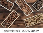 Various types of nuts, cinnamon and rusty bells on small teak trays on a natural wooden background. Top view. Natural banner. Autumn and Advent or Christmas background. 