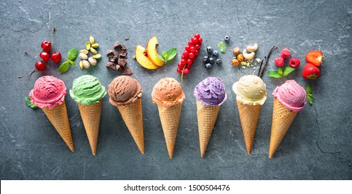 Various Varieties Of Ice Cream In Cones With Mint, Blueberry, Strawberry, Pistachio, Cherry And Chocolate On Grey Stone Background