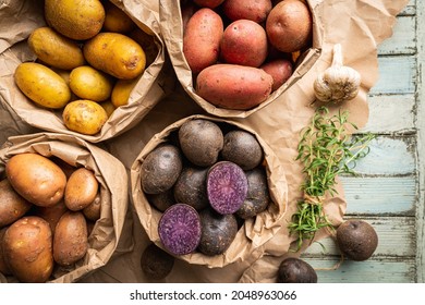 Various varieties of new colorful, white, red and purple potatoes in paper bags on white wooden background, top view - Powered by Shutterstock