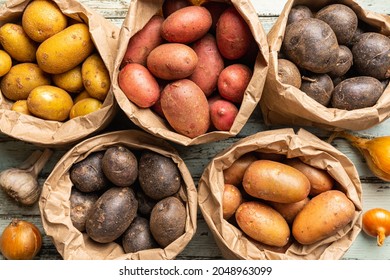 Various varieties of new raw colorful, white, red and purple potatoes in paper bags on white wooden background, top view