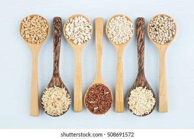 Various varieties of rice and wholegrains in spoon on wooden table background. Wheat, barley, millet, oats, rice, coarse grain, sorghum, lotus seed.