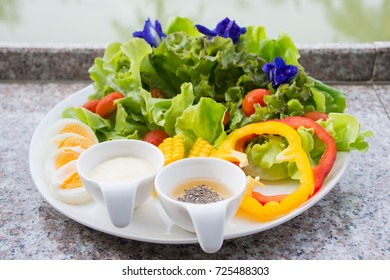 Various vegetable and egg or salad in white bowl with a pair of salad cream cups on mable table