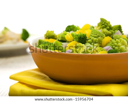 various vegetables in clay bowl, broccoli, romanesco, yellow carrot slices, green beans, red onion pieces