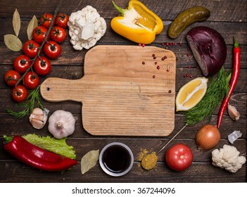 Various vegetables and spices and empty old cutting board. Colorful ingredients for cooking on rustic wooden table around empty cutting board with copyspace. Top view. Retro styled.