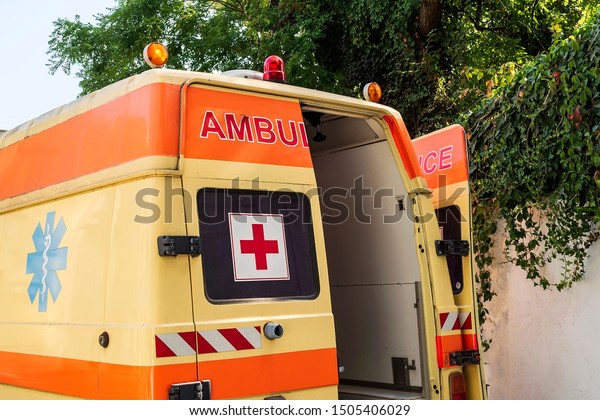 Varna, Bulgaria, September 13, 2019. Stationary\
yellow ambulance car with red cross on the windows. An emergency\
medical service van with opened back door. On a sunny summer day.\
Rear view.