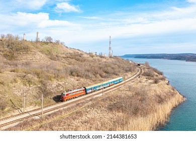 Varna, Bulgaria - Spring 2022: A Red Electric Locomotive Pulls The Carriages Of An Intercity Passenger Train Along The Railway Line On The Black Sea Coast. Aerial View. Bulgarian Railway