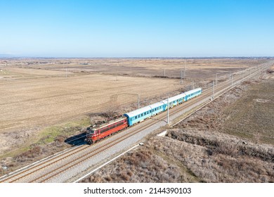 Varna, Bulgaria - Spring 2022: Red Color Electric Locomotive Pulls The Carriages Of An Intercity Passenger Train Along The Railway Line. Aerial View. Bulgarian Railway