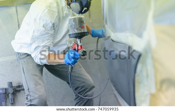 A varnisher is painting a bodywork of a car\
with a spray gun. No face but dust\
mask