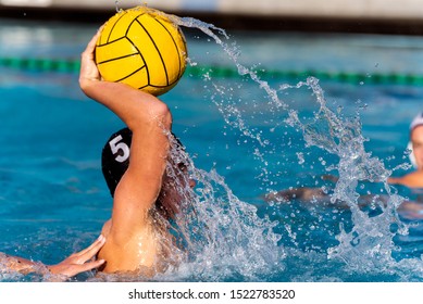 Varsity Water Polo Player In Black Cap Number 5 Is Bringing Up Ball For Shot On Goal With Trail Of Splashing Water Showing His Power.