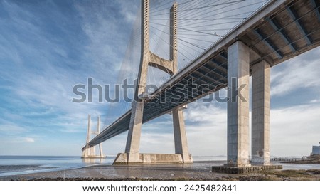 Vasco da Gama bridge timelapse hyperlapse with reflection on water and blue cloudy sky. Cable-stayed bridge and Tagus river. Lisbon, Portugal.