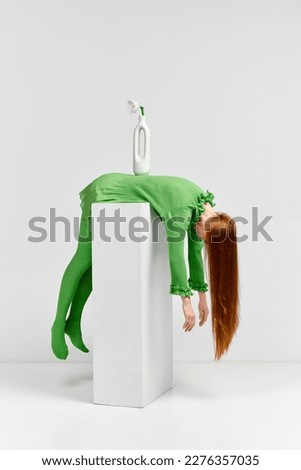 Vase. Avant-garde and experimental art style of human portrait. Beautiful woman with long glossy healthy red hair in green outfit over light background. Body language, impersonal emotions concept