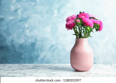 Vase with beautiful aster flower bouquet on table against color background. Space for text