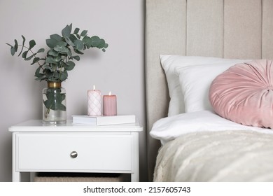 Vase With Beautiful Eucalyptus Branches, Book And Candles On Nightstand In Bedroom