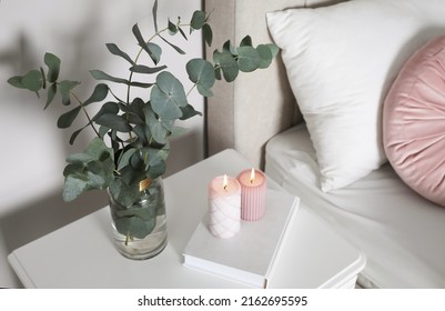 Vase With Beautiful Eucalyptus Branches, Book And Candles On Nightstand In Bedroom