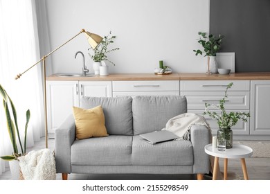 Vase with blooming tree branches and sofa with modern laptop in light room interior