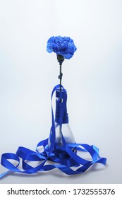 It Is A Vase With A Blue Carnation By Winding A Blue Ribbon Around A Glass Bottle.
