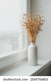 Vase of dried flax linum on windowsill. Nordic style home interior decor.