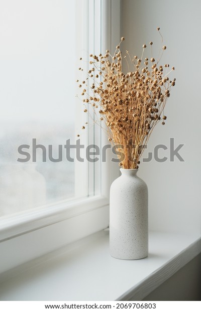 Vase of dried flax linum on windowsill. Nordic
style home interior decor.