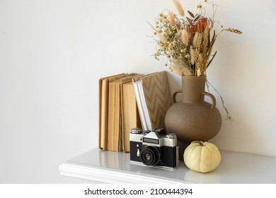 Vase With Dried Flowers, Pumpkin, Photo Camera And Books On Mantelpiece Near Light Wall