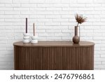 Vase with dried red protea and candles on dresser near white brick wall