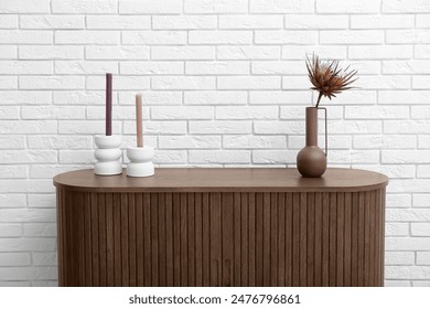 Vase with dried red protea and candles on dresser near white brick wall