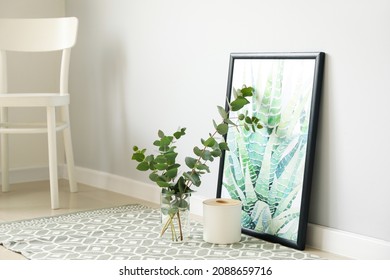 Vase with eucalyptus branches and picture near light wall
