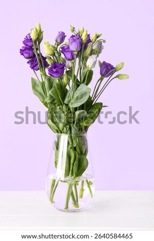 Vase with eustoma flowers on table near lilac wall