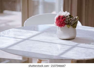Vase filled with fake flowers on a white marble table with sunshine. Still life decor in a room. Home Decorations.