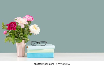 
Vase Of Flowers And A Row Of Books With Glasses For Vision On A White Wooden Table