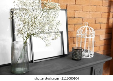 Vase With Gypsophila Flowers And Blank Frames On Mantelpiece Near Brick Wall