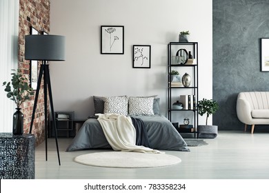 Vaas op metalen tafel en grijze lamp in ruime slaapkamer met wit tapijt en galerij op muur boven bed